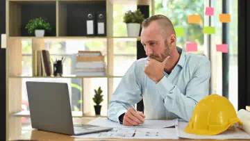 Man sits at a desk and looks at a laptop