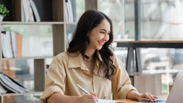 Woman uses a computer and takes notes on a piece of paper